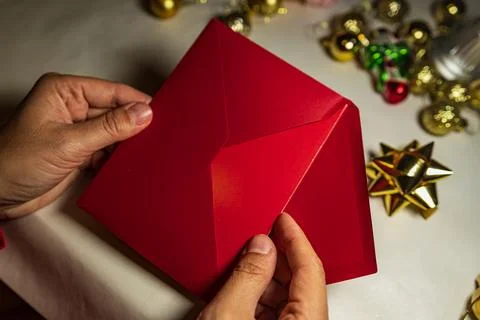 Hands opening red Christmas envelope with holiday decor Stock Photos