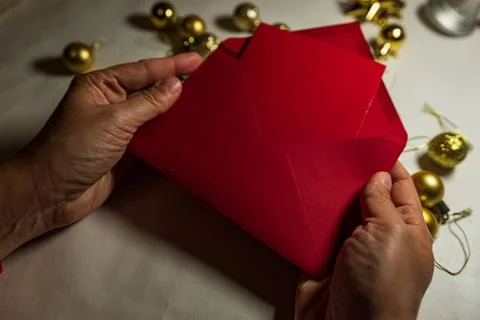 Hands opening red Christmas envelope with holiday decor Stock Photos