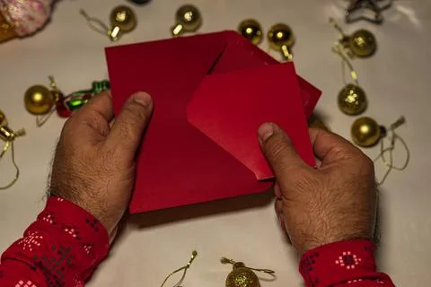 Hands opening red Christmas envelope with festive ornaments Stock Photos