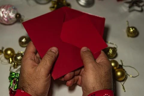 Hands opening red Christmas envelope with holiday decor Stock Photos