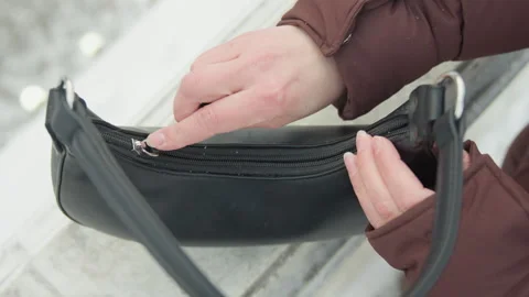 Hands opening small black leather shoulder purse with zipper over tiled surface Stock Footage 345652539