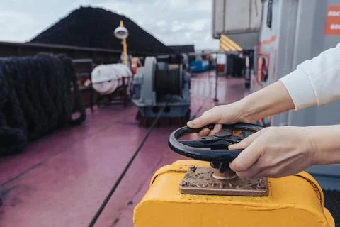 Hands operate control valve on ship deck during coal loading in busy port Stock Photos