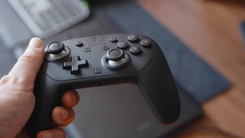 Hands Operating Black Game Controller Indoors Near Laptop Computer Stock Footage 345692569