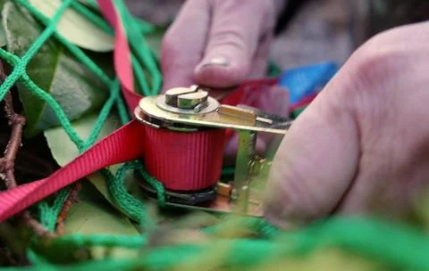 Hands operating a ratchet tie-down strap mechanism Stock-Fotos