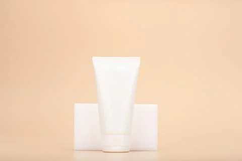 Hands or face cream in white glossy tube against light beige background Stock Photos