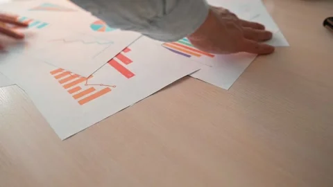 Hands organize and sort various papers filled with charts and graphs on a wooden Stockbeeldmateriaal 338303235