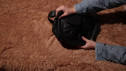Hands organizing a black leather handbag on a fluffy brown carpet background Stock Footage 339177217