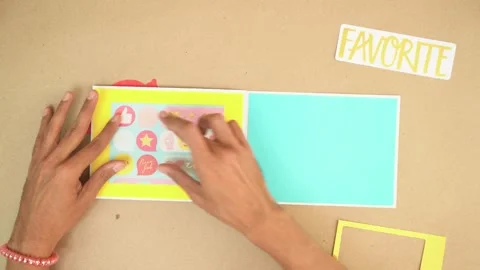 Hands pasting colorful paper elements onto scrapbook page with decorative Stock Footage 289288651