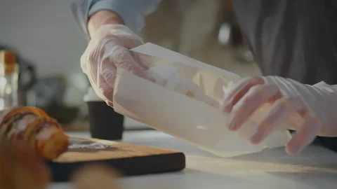 The hands of pastry chef pack fresh croissants into paper bag to be given to Stock Footage 270385994