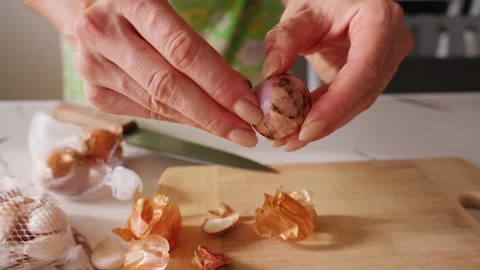 Hands Peel a Small Onion over a Wooden Cutting Board in a Kitchen, Preparing Fre Stock Footage 341974207