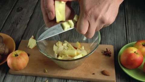 Hands peeling and chopping apples into a glass bowl on a wooden table with fresh Stock Footage 339366878