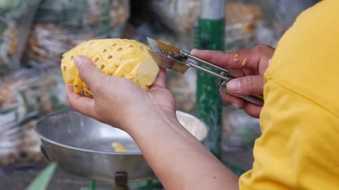 Hands peeling and trimming a pineapple at a market stall with a metal bowl on th Stock Footage 338001730