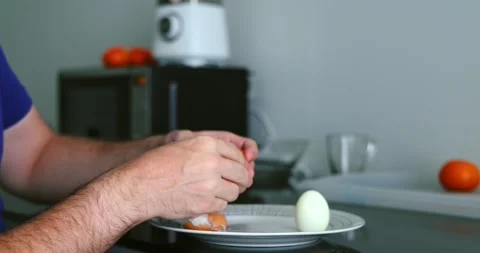 Hands peeling boiled egg on kitchen counter, oranges in background, Stock Footage 305936168