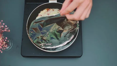 Hands peeling foil to reveal cheesy pizza in frying pan in kitchen Видео 342882753