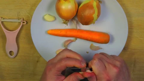 Hands peeling garlic on white plate with onions carrot peeler Stock Footage 345421986
