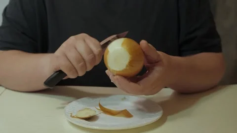 Hands peeling onion with small knife over white plate Vidéo 342362186