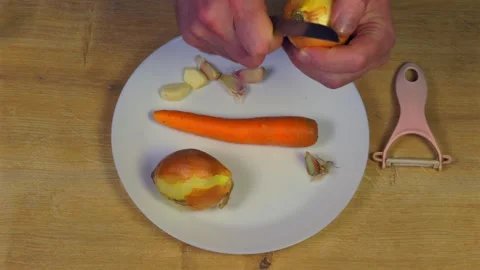Hands peeling onion on white plate with carrot garlic peeler Stock Footage 345421998