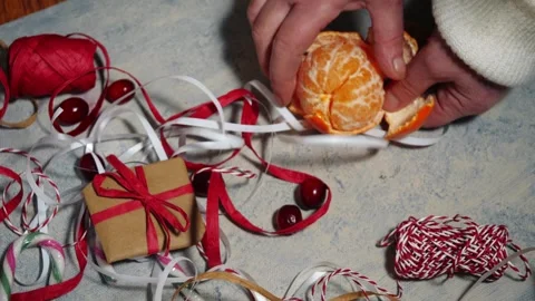 Hands peeling orange fruit with red and white Christmas gifts and wrapping Stock Footage 326359579