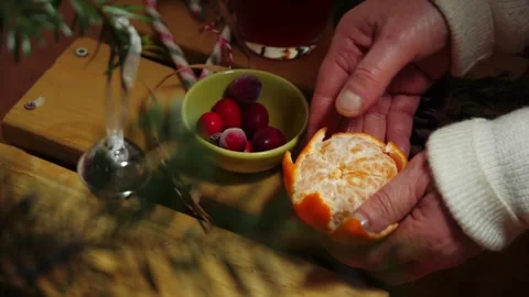 Hands peeling orange fruit through view of Christmas tree Stock Footage 325448330