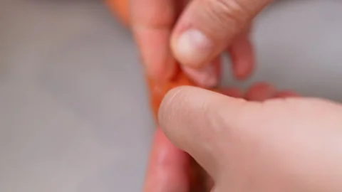 Hands peeling orange plastic casing from a pink sausage on a gray surface Stock Footage 346799878