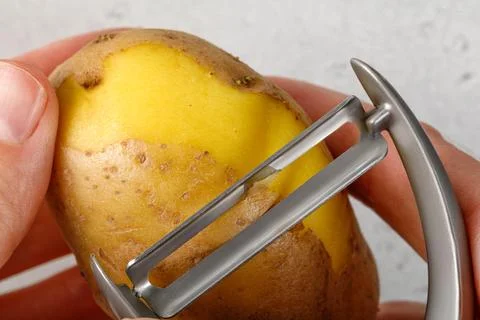 Hands peeling a potato with vegetable peeler, Close up. Kitchen working. Pr.. Stock Photos