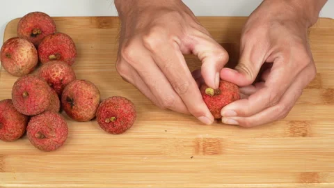 Hands Peeling Ripe Red Lychee Shell on Wooden Chopping Board Stock Footage 337326378