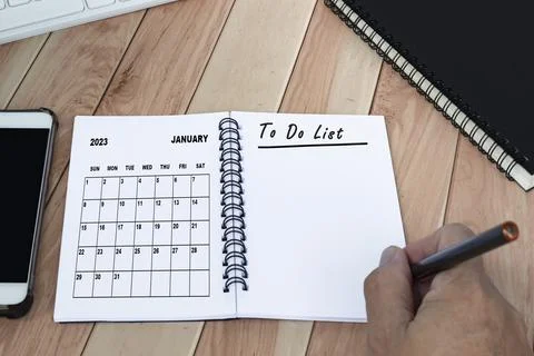 Hands with pen writing to do list with January 2023 calendar on notebook. 库存照片