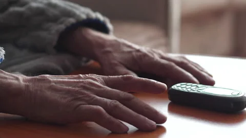 Hands of a pensioner on the table next to a push-button mobile phone. the c.. 스톡 동영상 232751701