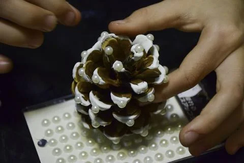 Hands of a person carefully decorating a pine cone with white paint and pea.. Фото