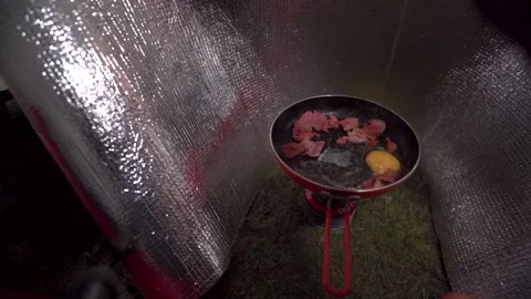 The hands of a person cracking eggs into a frying pan while camping 動画素材 263962686