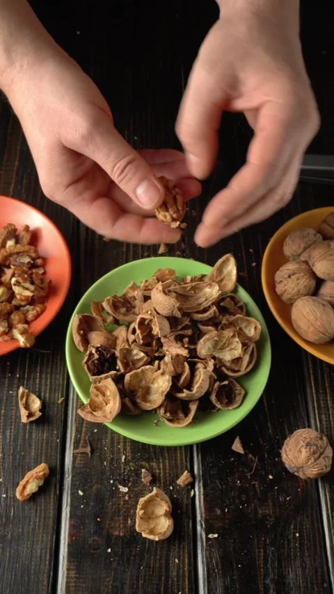 Hands of a person cracking open walnut shells over a green bowl filled with Stock Footage 328090594