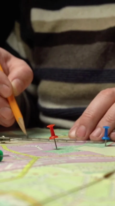 Hands of a person marking locations on a map with colored push pins and a Stock Footage 338131437