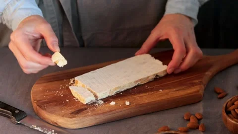 A hands pick up a freshly broken piece of hard Spanish Turron de Alicante, a  Stock Footage 331378924