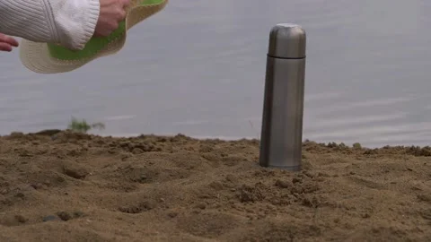 Hands pick up straw hat and thermos flask from beach Stock Footage 167889311