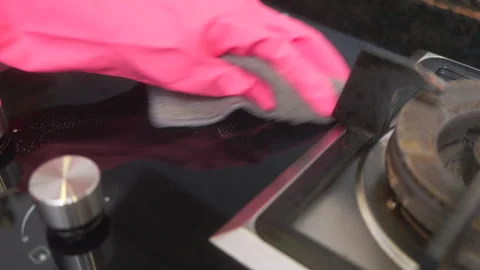 Hands in pink rubber gloves cleaning a black gas stove with a microfiber cloth. Stock Footage 328924062