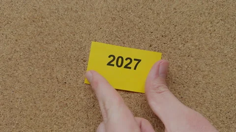 Hands pinning a yellow note with the year 2027 on it. Stock Footage 329640380