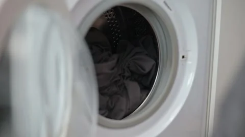 Hands place and retrieve fabric items from a front-loading washing machine in a Видео 337101423