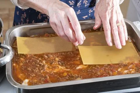 Hands place lasagna sheets over rich meat sauce Stock Photos