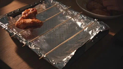 Hands place marinated chicken wing on foil-lined rack for baking Stock Footage 312647916