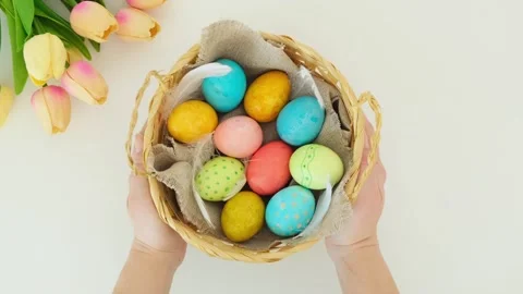 Hands place a wicker basket with multi-colored Easter eggs on a white table Stock Footage 331499529
