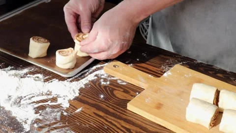 Hands placing cinnamon roll dough portions on baking tray for proofing on Stock Footage 310337454