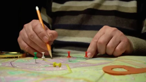 Hands placing colored pins on a detailed map while using a pencil for marking Stock Footage 333104653