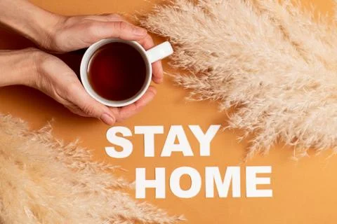 Hands placing cup of tea next to stay home message laid on an orange surface Stock Photos