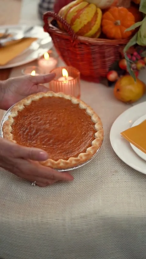 Hands placing a freshly baked pumpkin pie on a rustic Thanksgiving dinner table. Stock Footage 344016834