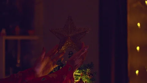 Hands Placing a Glittering Star on Top of a Decorated Christmas Tree With Warm F Stock Footage 338194703