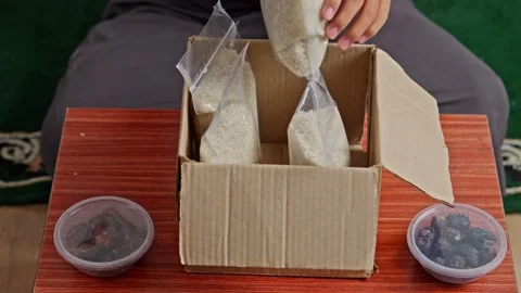 Hands placing plastic bags of raw rice into box for zakat al-fitr distribution Stock Footage 328987028