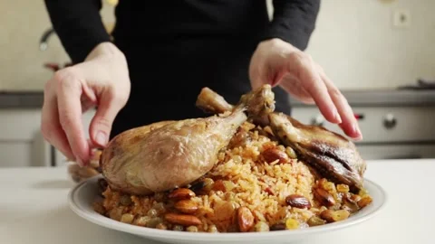 Hands placing a roasted chicken quarter onto a platter of spiced rice with .. Видео 333638510