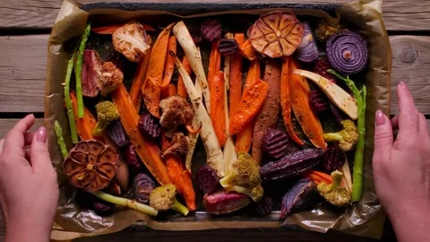 Hands Placing Roasted Vegetables Tray on Table for Sunday Roast Stock Footage 325897812