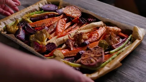 Hands Placing Roasted Vegetables Tray on Wooden Table for Sunday Roast Stock Footage 328094744