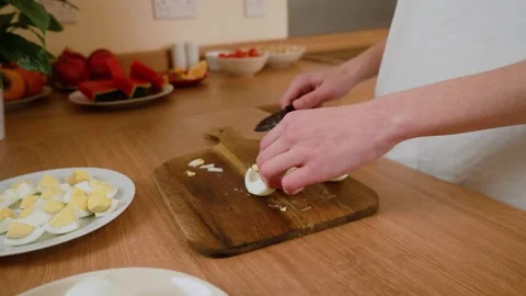 Hands placing sliced boiled eggs on wooden cutting board. Person arranging egg Stock Footage 303064189